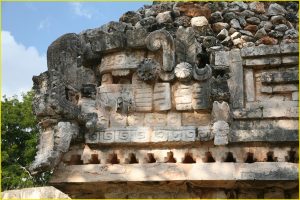 Human face peering out from between jaws of a serpent head on the facade of El Palacio, Labna
